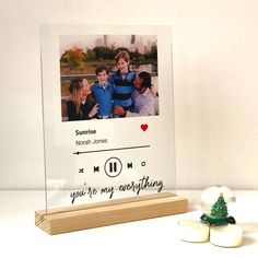 a glass photo frame sitting on top of a wooden stand next to two small christmas trees