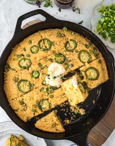 a skillet filled with cornbread and topped with green onions, cheese and jalapenos