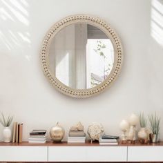 a white dresser topped with books and vases under a round mirror