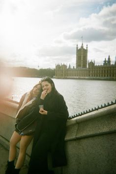 two women sitting next to each other on the side of a bridge over looking water