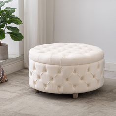 a white ottoman sitting on top of a rug next to a potted plant