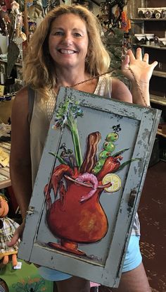 a woman holding up a painting in a shop