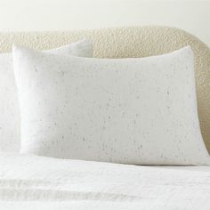 two white pillows sitting on top of a bed next to a pillow case with black speckles