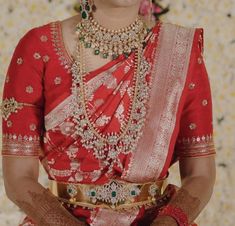 a woman in a red and gold sari with jewelry on her neck, sitting down