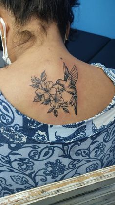 a woman with a bird and flowers tattoo on her upper back neck, looking down at the ground