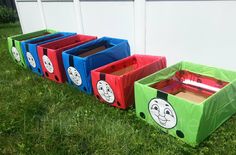 three boxes with faces painted on them sitting in the grass next to a white wall