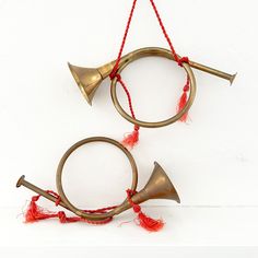 two brass wind chimes hanging from strings on a white wall with red tassels