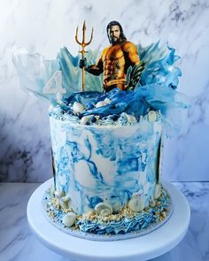 a blue and white cake with a figure on top is sitting on a marble table