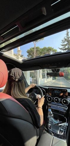 two people driving in the back seat of a car on a road with trees and buildings behind them