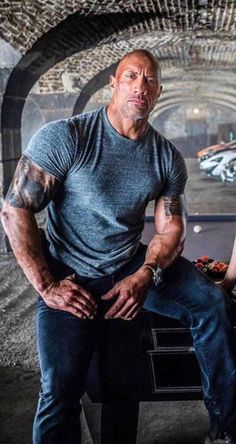 the rock sitting on a bench with his hands in his pockets