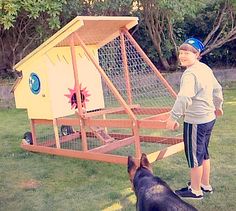 a woman standing next to a dog on top of a grass covered field near a chicken coop