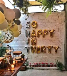 an outdoor birthday party with balloons, cake and decorations on the table in front of a brick wall