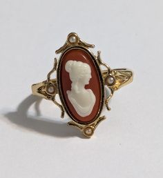 Vintage AVON Lady Face Cameo band Ring 1978 This is a traditional oval cameo of the white lady on a coral background set in delicate gold filigree. The ring has an inner adjustable ring and fits sizes 7 to 8.5 This 45-year-old item is in great new condition in its original box Vintage Cameo Oval Cabochon Rings, Vintage Cameo Ring With Oval Cabochon, Retro Oval Cabochon Jewelry, Vintage Oval Cameo Ring, Vintage Adjustable Cameo Rings, Retro Cameo Jewelry For Formal Occasions, Formal Retro Cameo Jewelry, Athena Jewelry, Lady Face