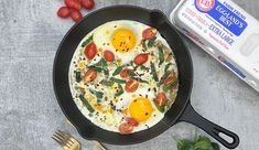 an omelet with eggs, tomatoes and spinach on the side next to a carton of yogurt