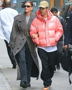 a man and woman walking down the street in winter clothes, one wearing a pink puffer coat