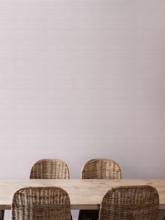 a wooden table with wicker chairs in front of a white wall and pink walls