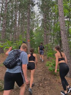 four people hiking in the woods with backpacks on their back and one person taking a photo