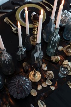 a table topped with lots of candles next to plates and silverware on top of a black table cloth