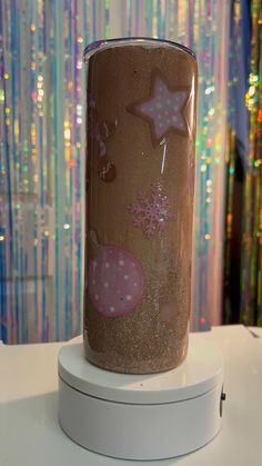 there is a cup with stars on it sitting on a stand in front of a curtain