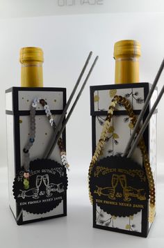 two wine bottles are decorated with gold, silver and black items as well as chopsticks