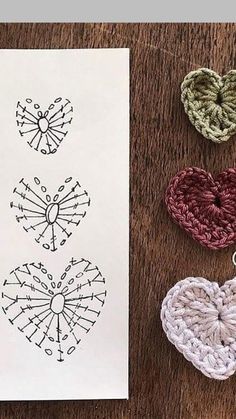 four crocheted hearts sitting on top of a table next to a piece of paper