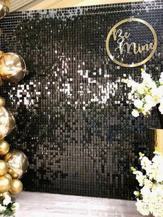 a black and gold wall decorated with balloons, flowers and vases in front of it