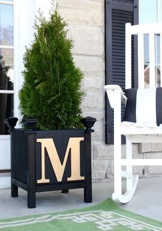 a white rocking chair sitting next to a potted planter with the letter m on it