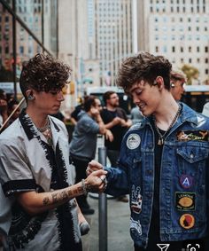 two young men standing next to each other in front of a group of people on a city street