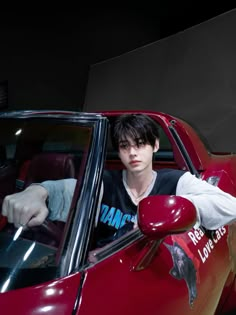 a young man sitting in the driver's seat of a red car with his hand on the steering wheel