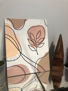 a painting on a table next to a vase with a plant in it and a wooden sculpture