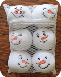 four snowman balls in a mesh bag on a wooden floor with the faces drawn onto them