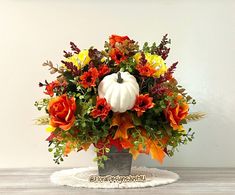 a white pumpkin sitting on top of a metal container filled with flowers and foliages