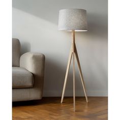 a wooden floor lamp next to a couch in a room with white walls and wood floors