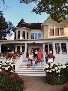 a group of people standing on the steps of a large house with flowers in front of it