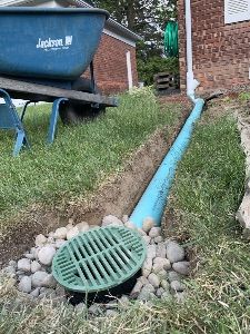 a drain in the ground next to a blue wheelbarrow and some green grass