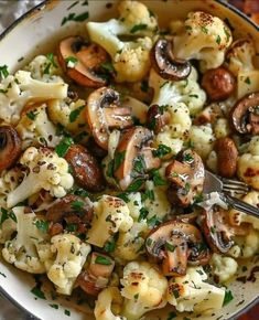 a bowl filled with cauliflower and mushrooms on top of a wooden table next to a fork