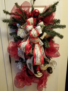 a red and white christmas wreath hanging on a door with bells, ornaments and ribbons