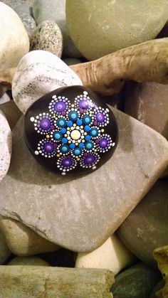 a painted rock sitting on top of a stone covered in white and purple dots next to another rock