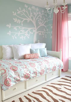 a bedroom decorated in blue and pink with a tree painted on the wall above the bed