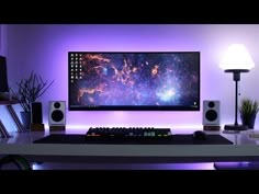 a computer desk with speakers and a large monitor on it's wall above the keyboard