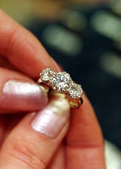 a woman's hand holding an engagement ring with three diamonds on top of it