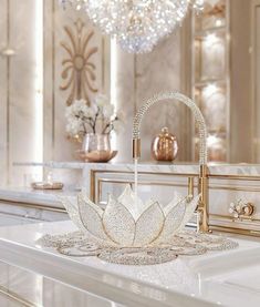 a white sink sitting under a chandelier next to a counter top with flowers on it