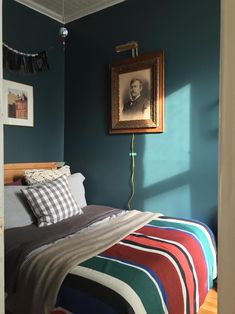 a bedroom with blue walls and striped bedspread, framed portrait on the wall