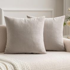 two pillows sitting on top of a couch next to a vase with flowers in it