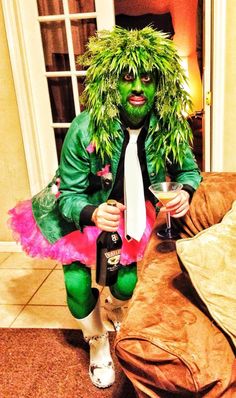 a man dressed in green and pink sitting on a couch with a wine glass next to him