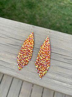 a pair of colorful beaded earrings sitting on top of a wooden table next to grass