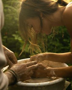 a woman is washing her hands in a bowl with dirt on the outside and trees behind it