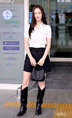 a woman standing in front of a building holding a black purse and wearing knee high boots