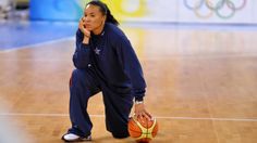 a woman sitting on the floor with a basketball in her hand and looking at something