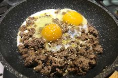 two eggs are being cooked in a skillet on the stove top with meat and cheese